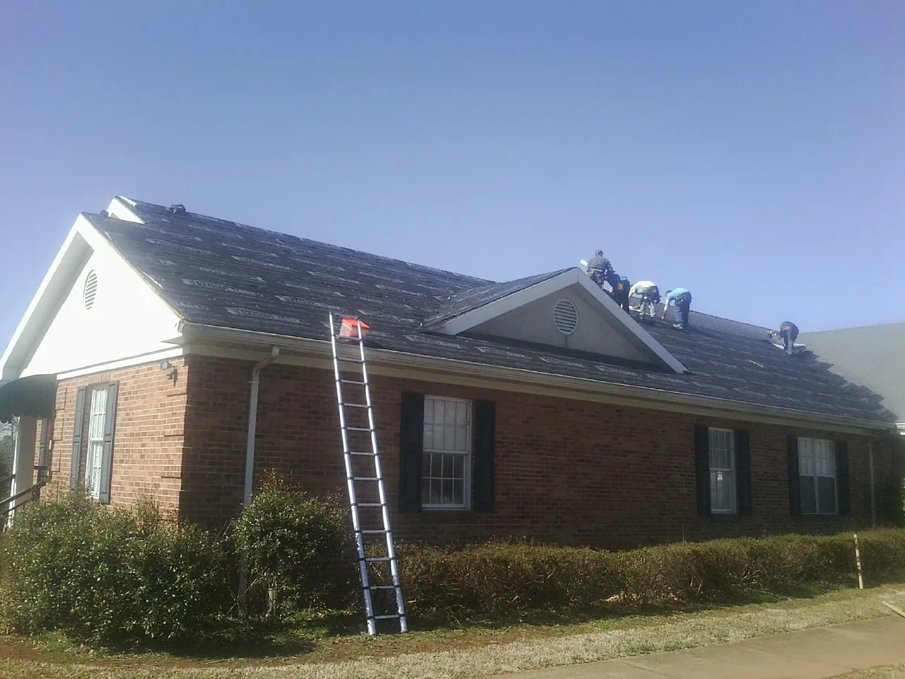 Crew tearing shingles off a brick ranch roof with a ladder set — Metal Roof Repair work by our crew in Groveport