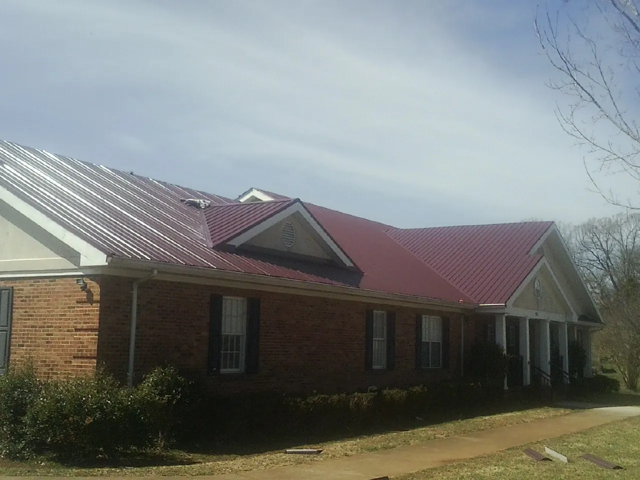 Red metal roof with gabled entries on a long brick building, from a Hail Damage Roof Repair job in Groveport