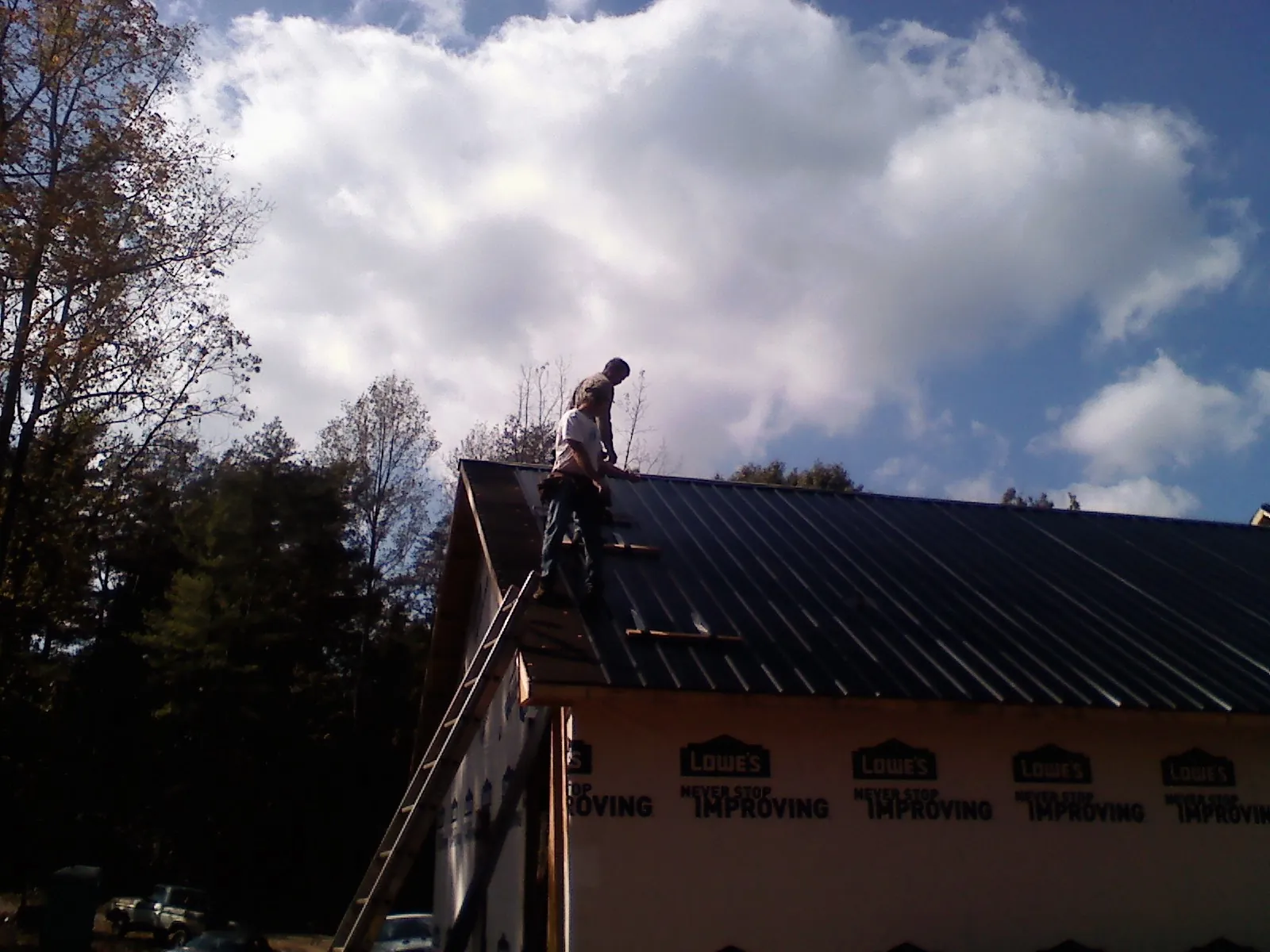 Roofer fastening dark metal panels high against a cloudy sky, from a Roof Inspection job in Groveport