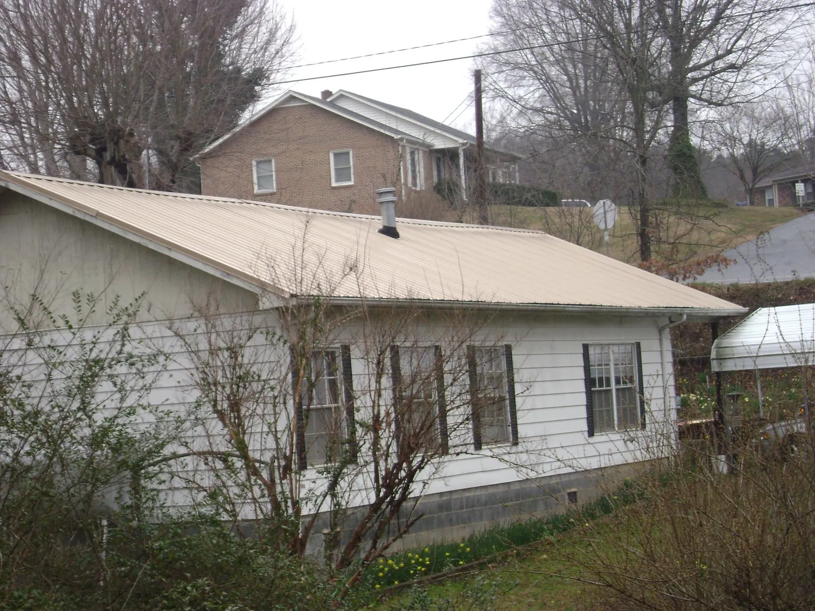Tan metal roof on a white sided house set into a hillside — Commercial Roofing by Roofing Brothers in Groveport